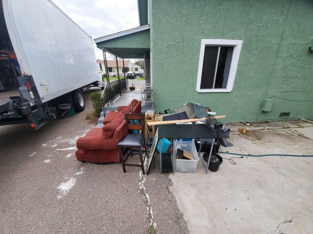 Furniture piled outside a green house beside a moving truck.