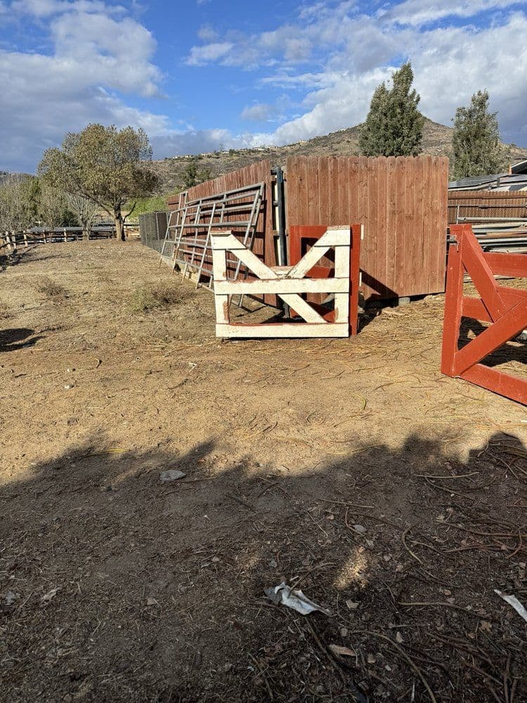 Wooden gate in a rustic farm setting with a fenced area and trees in the background.