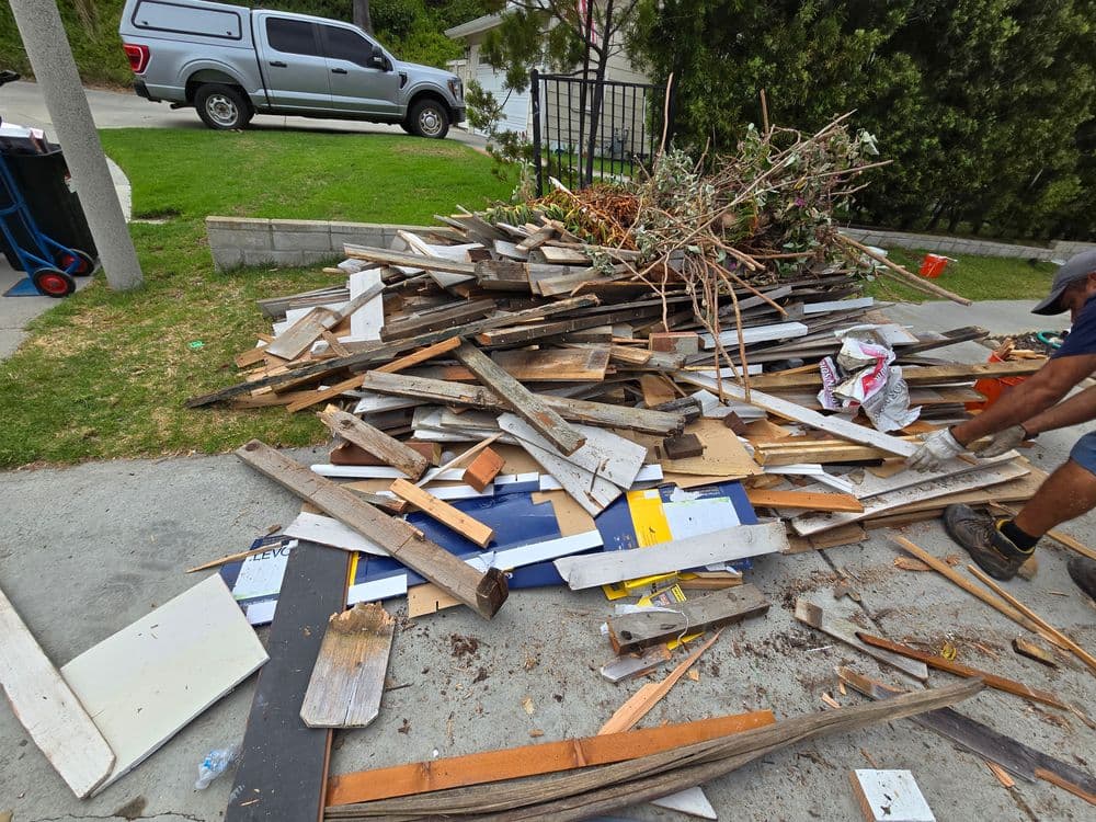Piled debris including wood, colorful signs, and vegetation in a residential area.